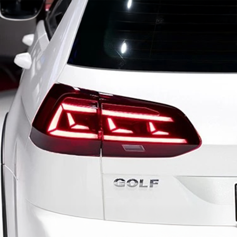 Close-up of the rear left taillight and trunk area of a white Volkswagen Golf, showing the illuminated red LED taillight and the silver GOLF badge.